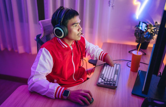 A disabled male gamer is wearing a headset and playing exciting online games in a neon-lit room.