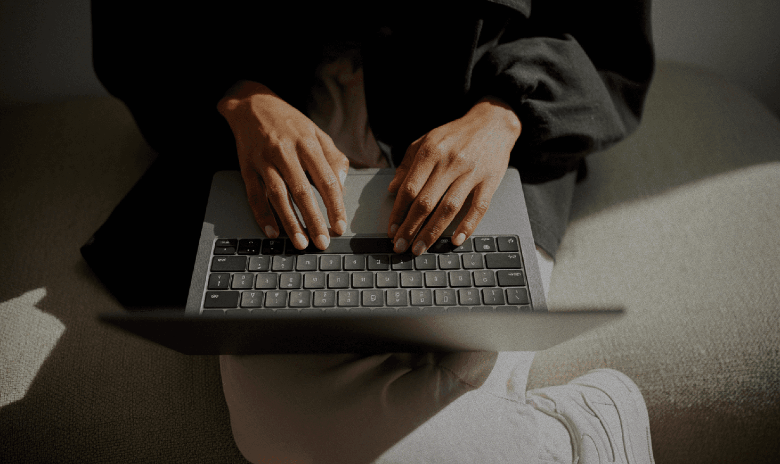 Osoba pisze na laptopie, siedząc na kanapie.