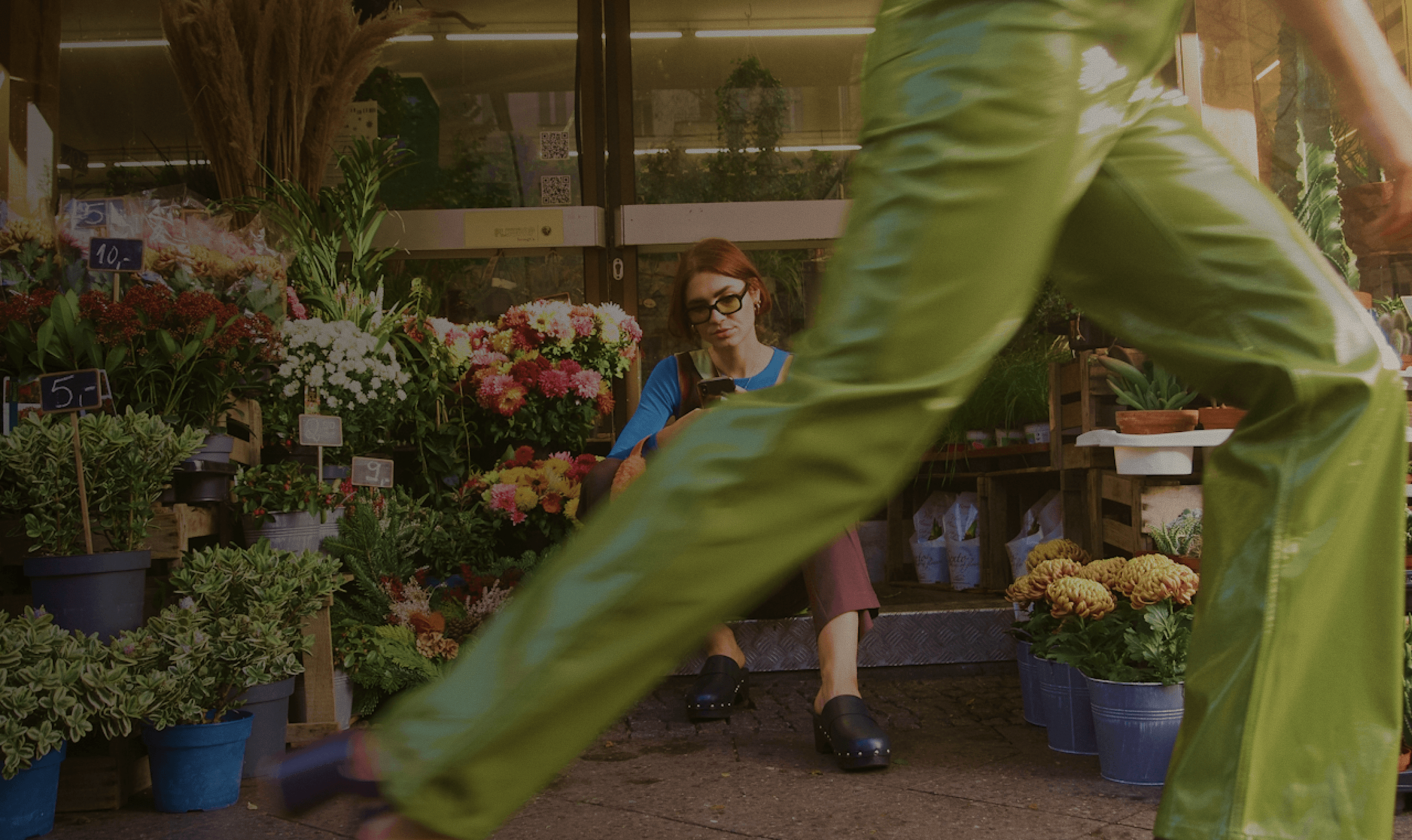 A person walks briskly past a vibrant flower stall filled with an array of colorful blooms and potted plants.