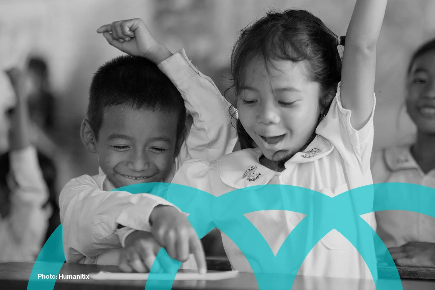 Young children excitedly raising their hands in a class room. (Photo courtesy of Humanitix)
