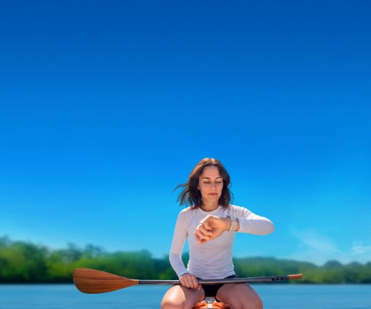 Žena sedí na paddleboardu a dívá se na chytré hodinky.